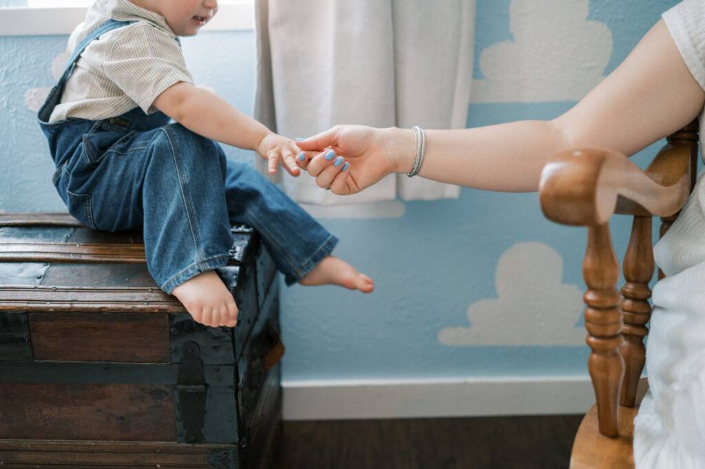 mom reaches for toddler's hand while holding newborn