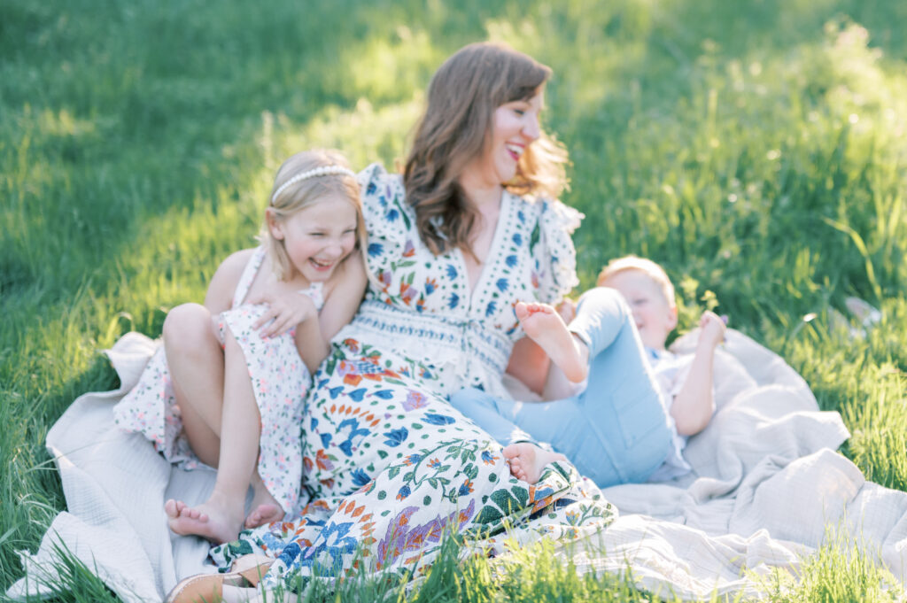 mom and kids laugh together while sitting in a field
