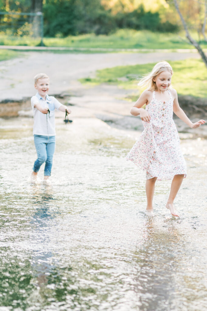 brother chases sister through a creek holding moss