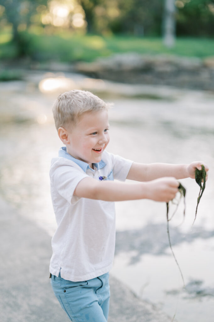 boy holds creek moss in hands while laughing