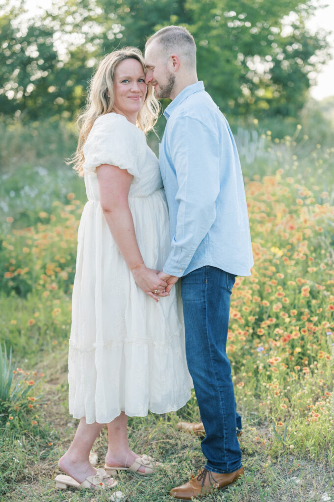 expecting parents stand in a field of flowers holding hands during maternity session