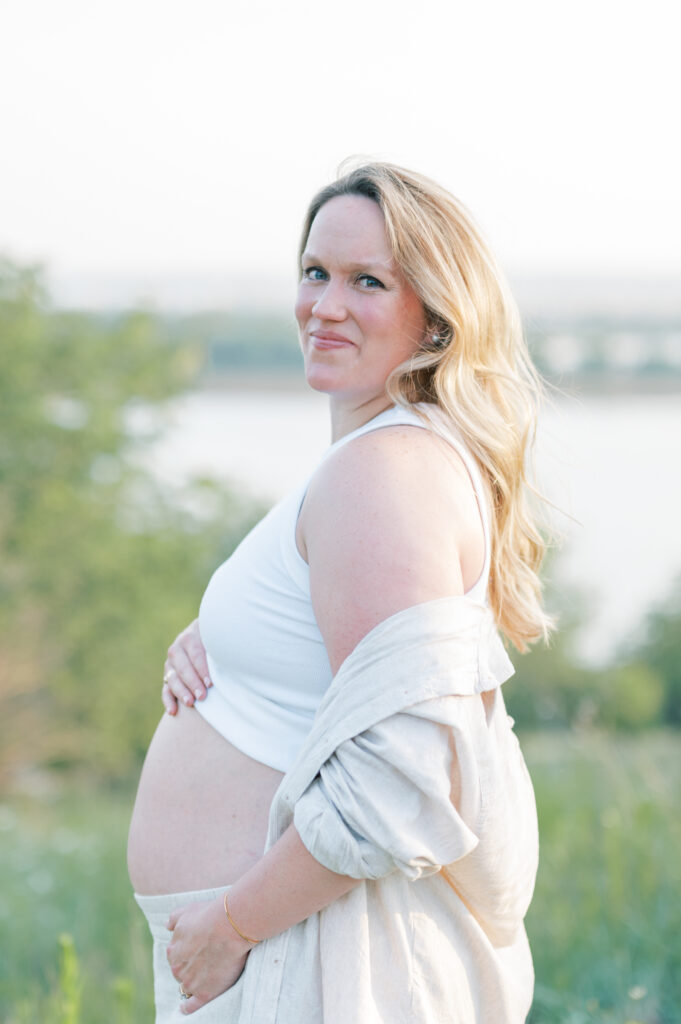 expecting mom embraces bump overlooking a Fort Worth lake during maternity session