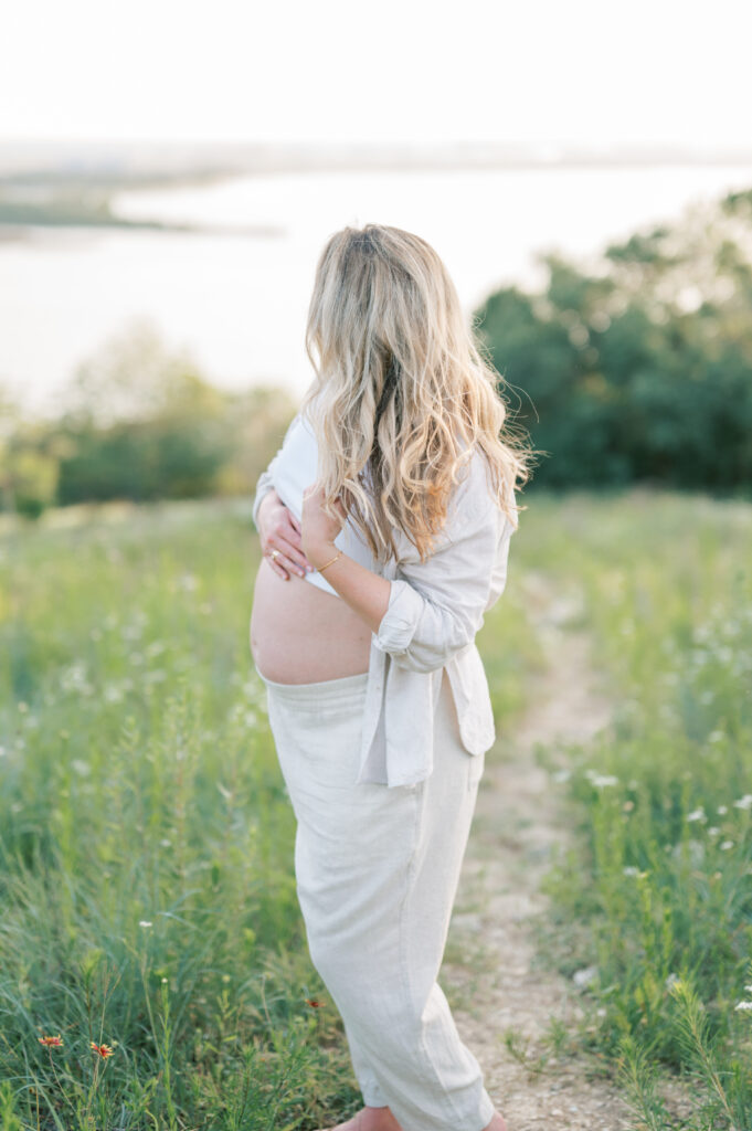 pregnant mom touches hair while looking out to a lake in Fort Worth during maternity session