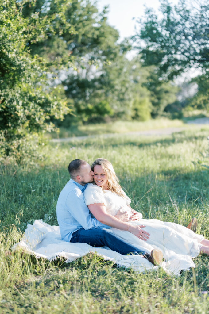 husband and wife snuggle close in a field