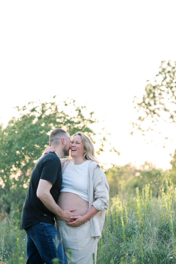 expecting parents hug  lovingly in a field at sunset