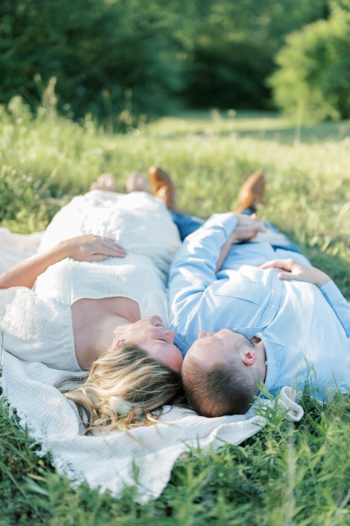 husband and wife lay in a field holding hands