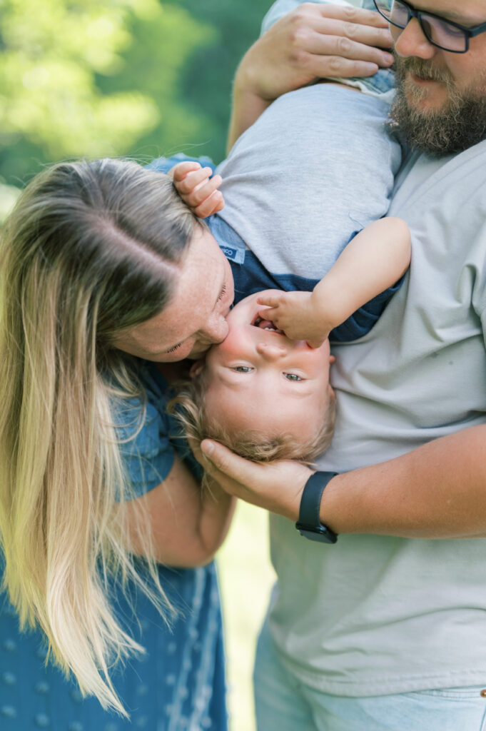 mom kisses toddler boy while dad holds him upside down
