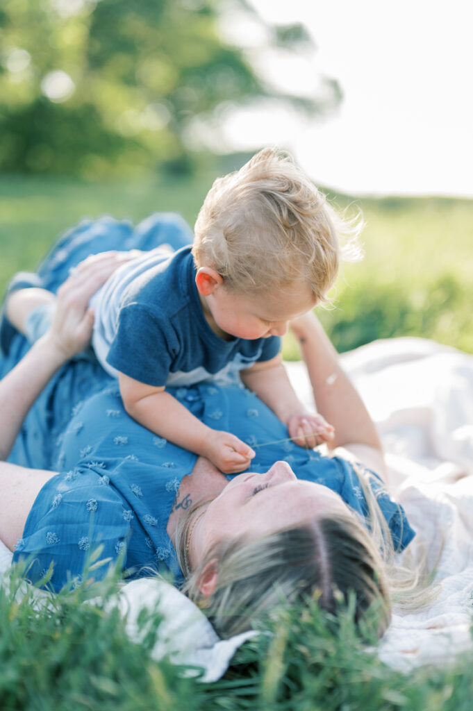 mom lays in grass with toddler son during family photo session 