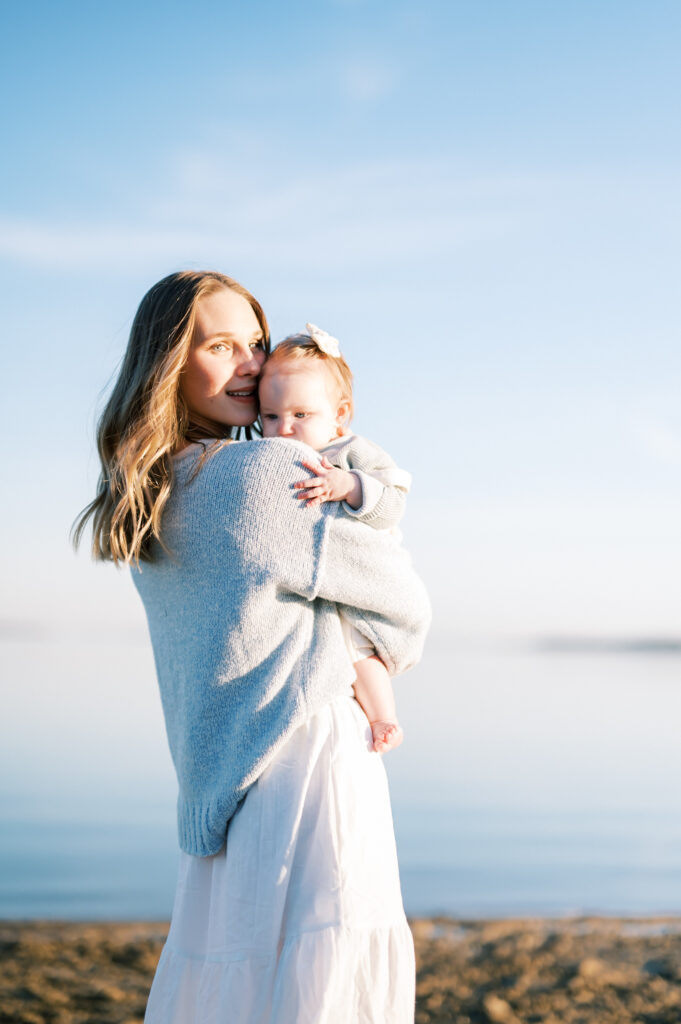 mom snuggles baby girl closely in sunlight