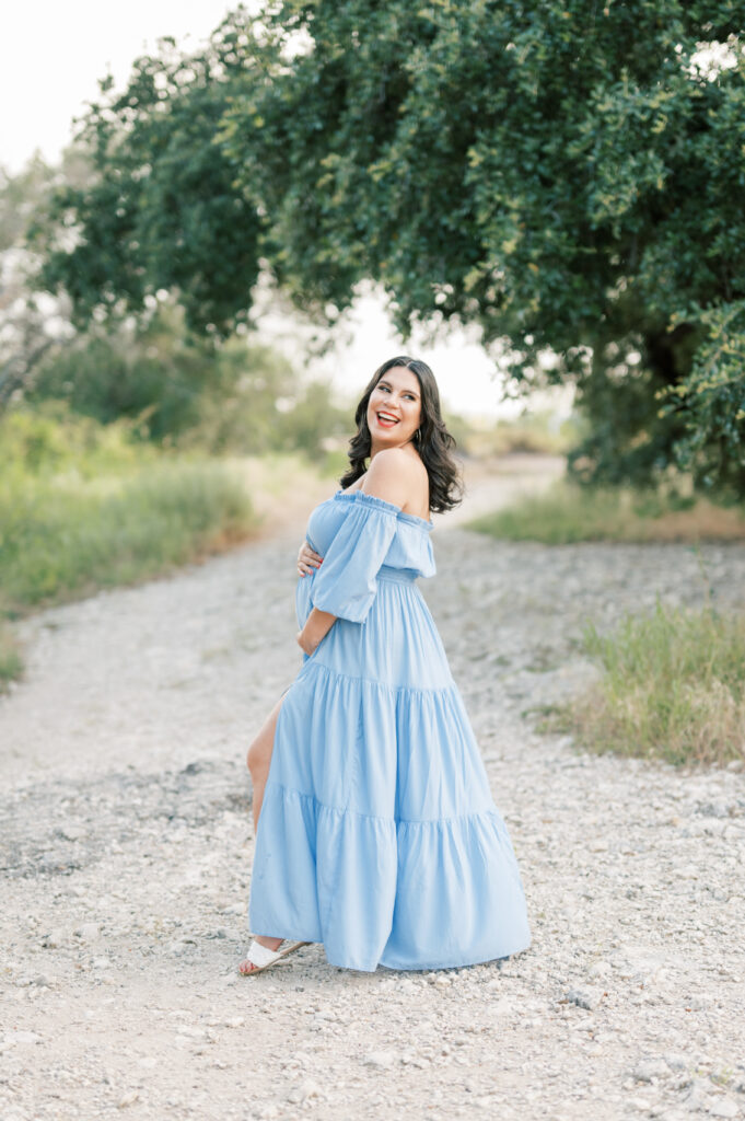 expecting mom stands under a tree smiling and holding baby bump