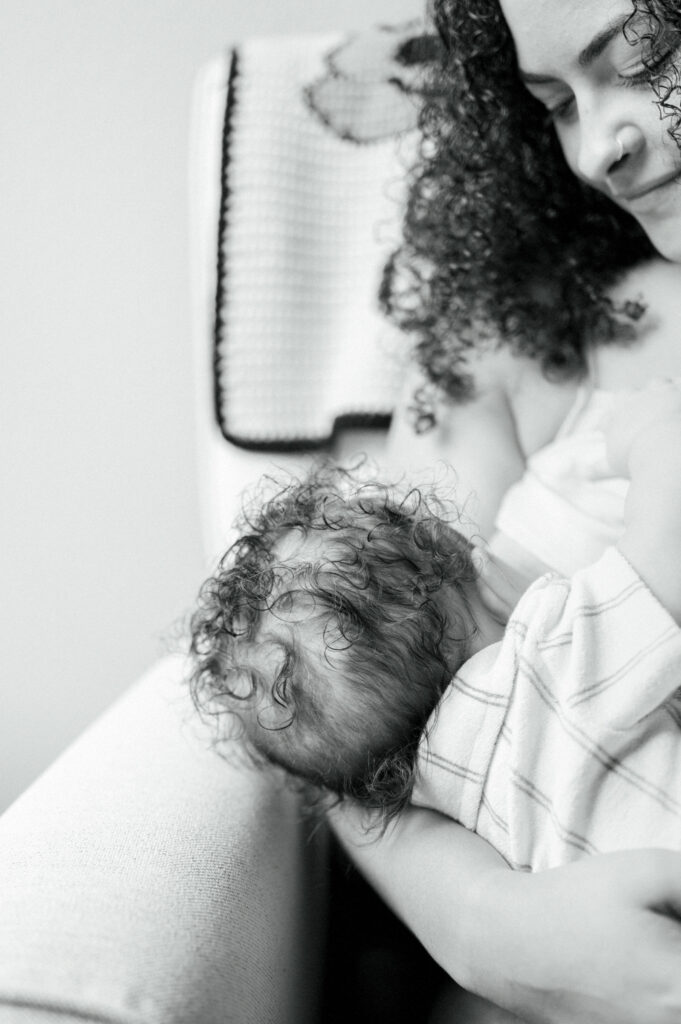 mom nurses baby boy while sitting on rocking chair