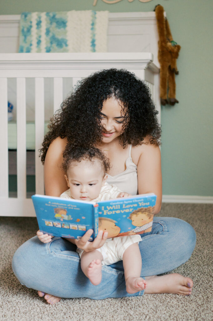 mom reads book to baby boy in nursery during milestone photos at-home