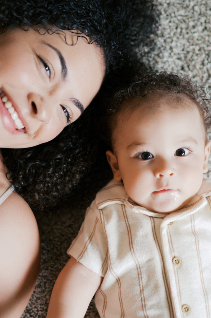 mom and baby boy lay on carpet and look up smiling