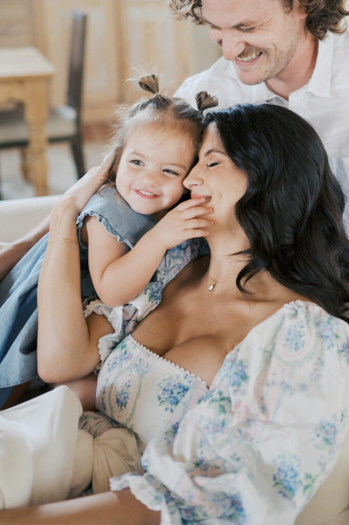 mom snuggles close with family and toddler girl while holding newborn