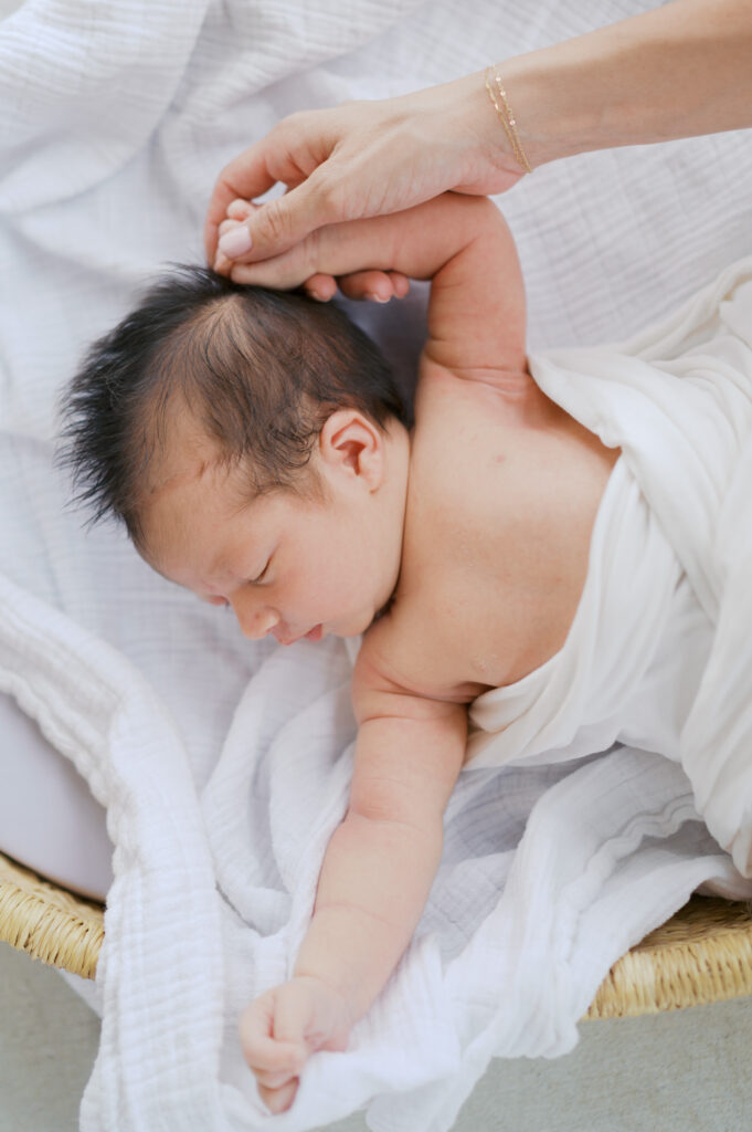 newborn baby stretches out while mom holds her hand