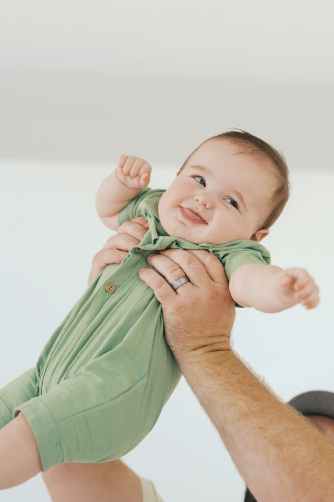 little boy laughs while held up in dad's arms