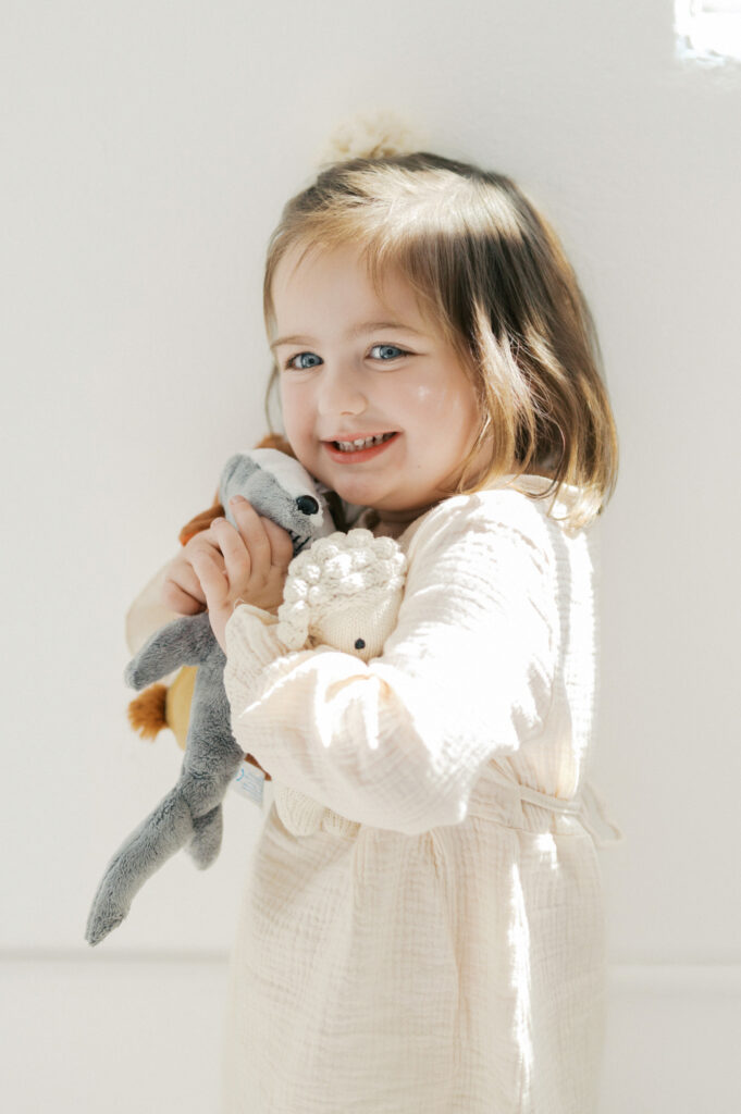 little girl smiles while holding stuffed animals in a studio