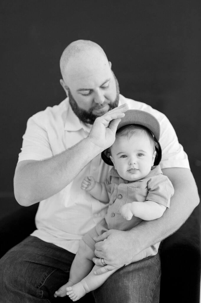 dad places baseball hat on little boy during family photos indoors