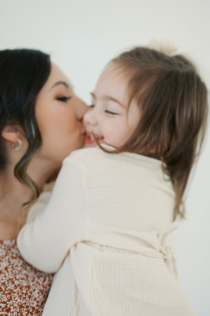 mom kisses cheek of little girl during family photos