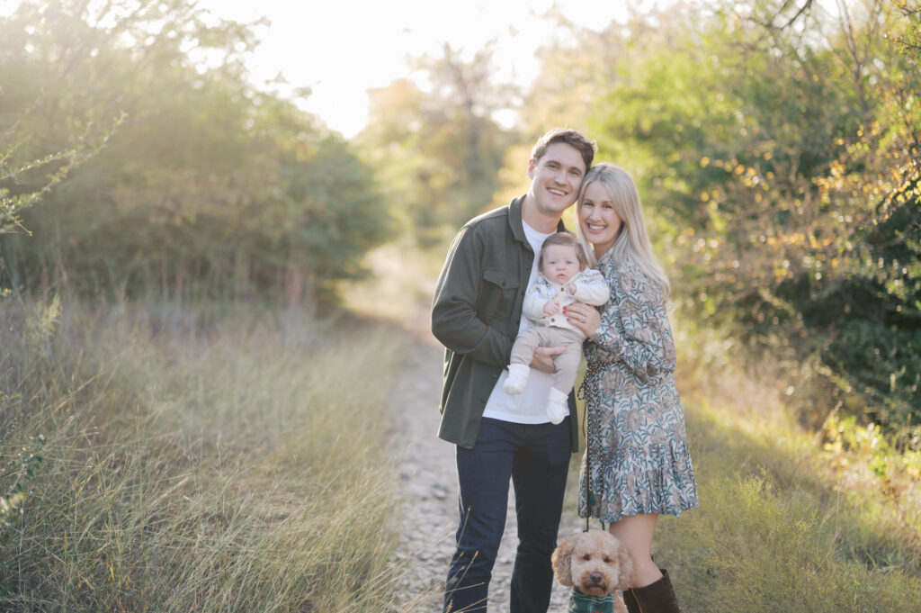 family of three and dog cuddle close for family photo