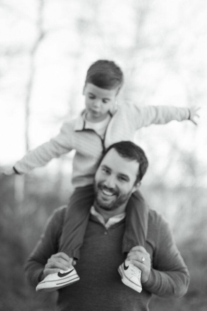 little boy rides on dad's shoulders like he is an airplane
