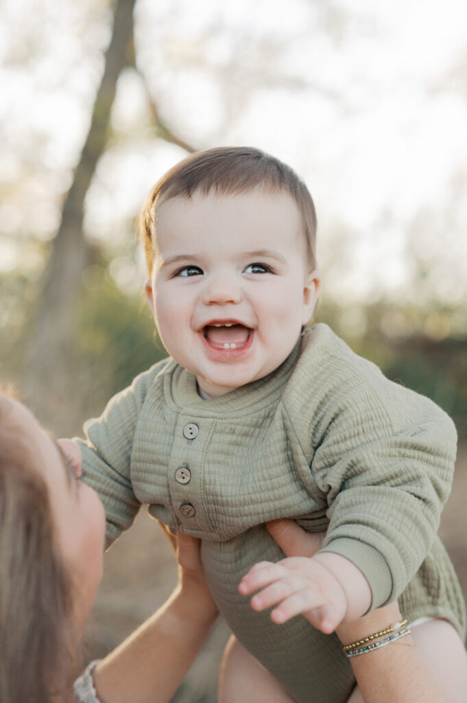 little boy smiles while mom holds him in air