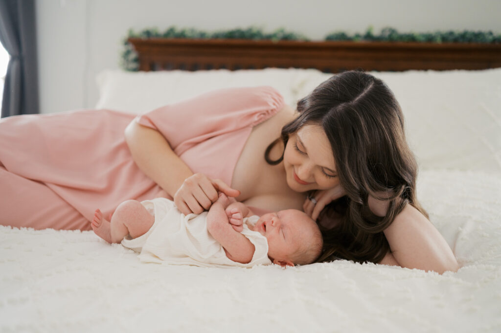 mom lays with newborn baby on bed