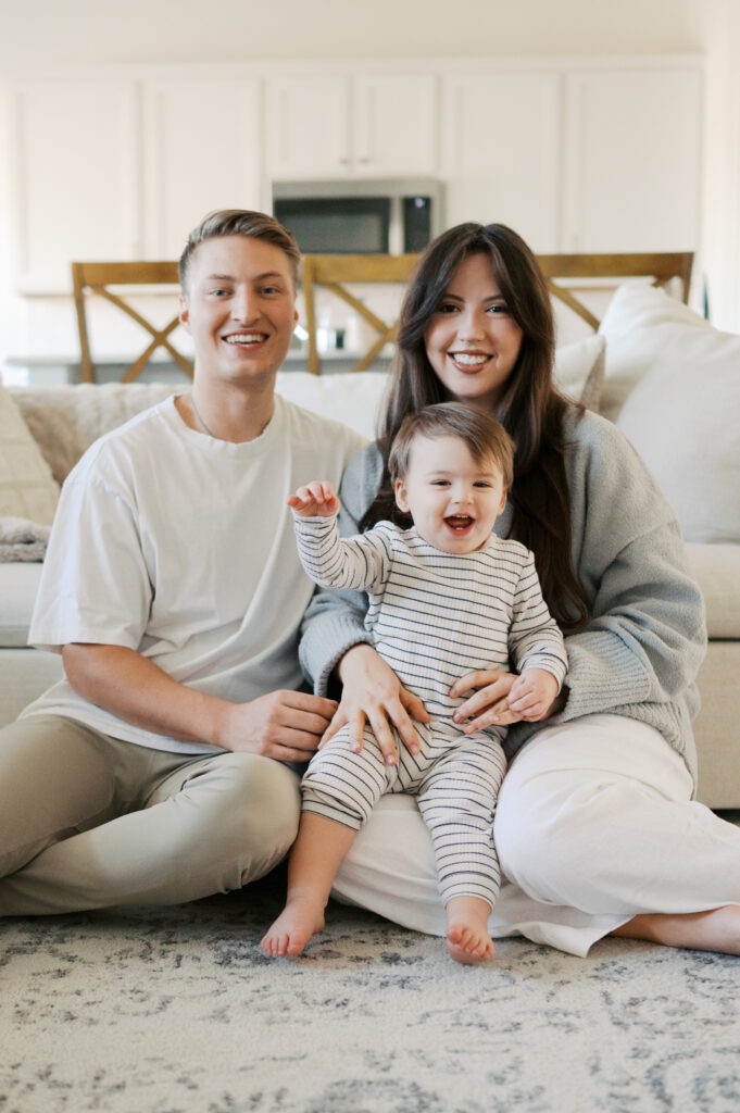 family of three and one on the way smiles together in living room
