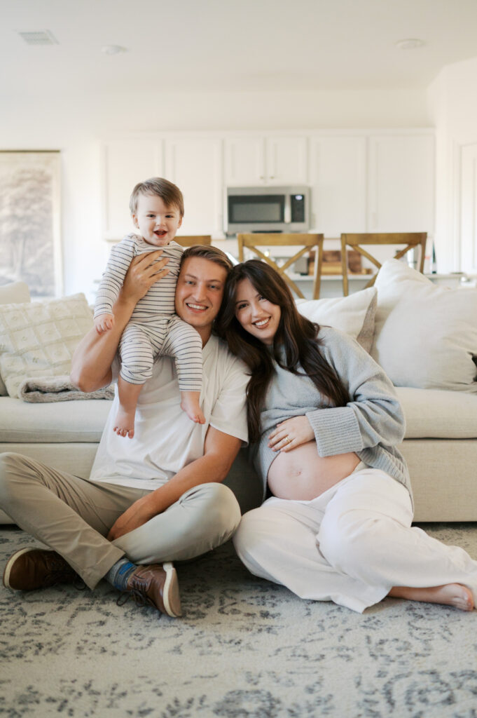 family of three smiles for a photo in living room during maternity photography session