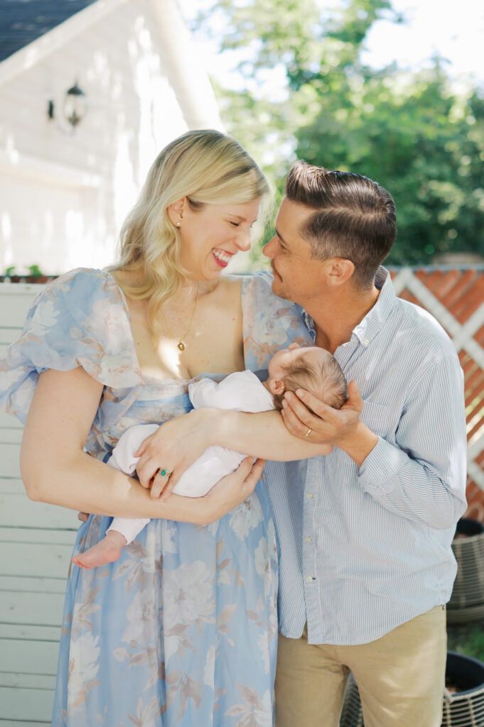 new parents smile at each other while holding newborn baby
