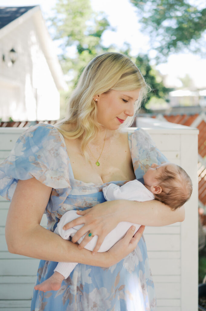mom looks adoringly at her newborn baby in backyard