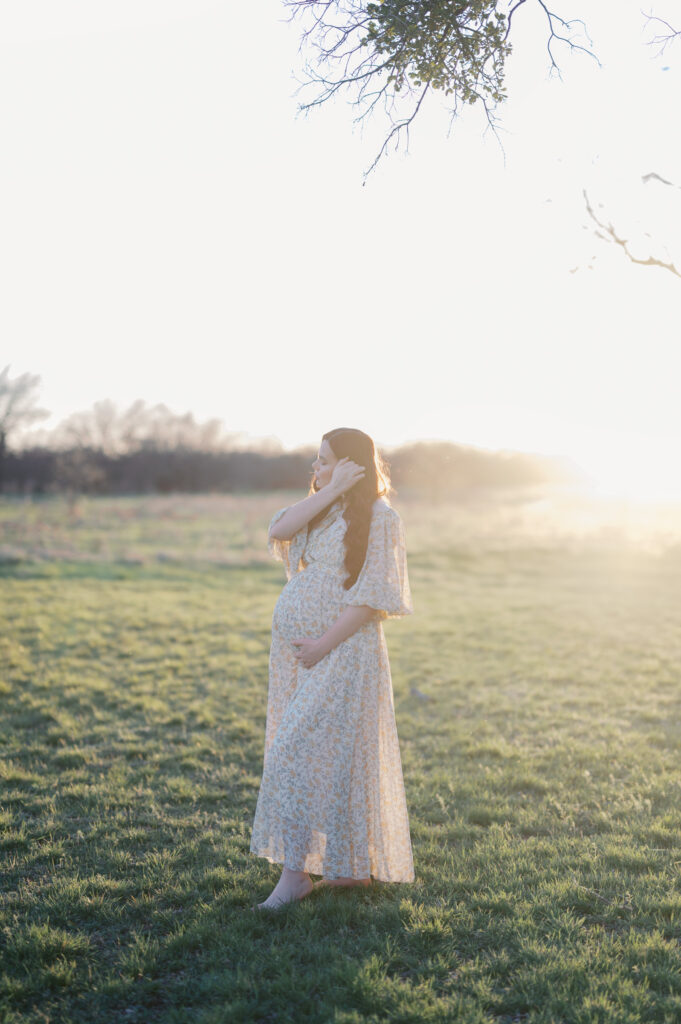 mom moves hair out of way while sun shines on her baby bump