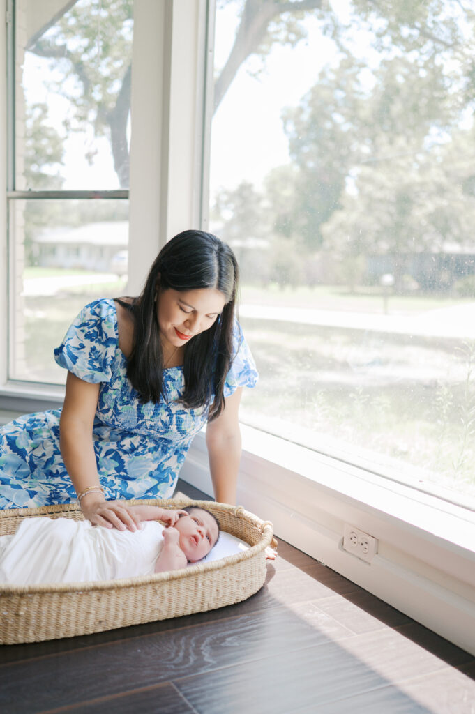 mom sits on ground with newborn baby while he lays in basket
