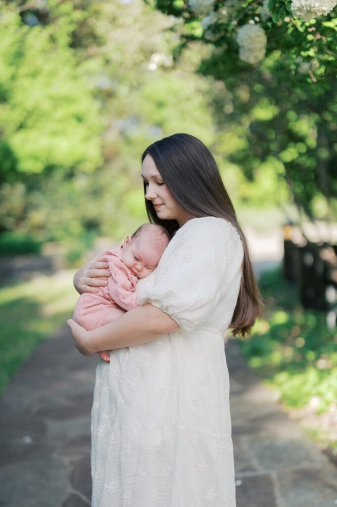 mom holds newborn baby outdoors at the fort worth botanic garden