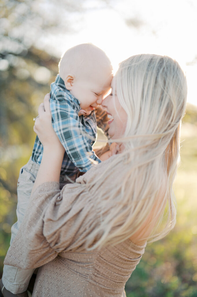 mom snuggles baby boy while sun shines behind them