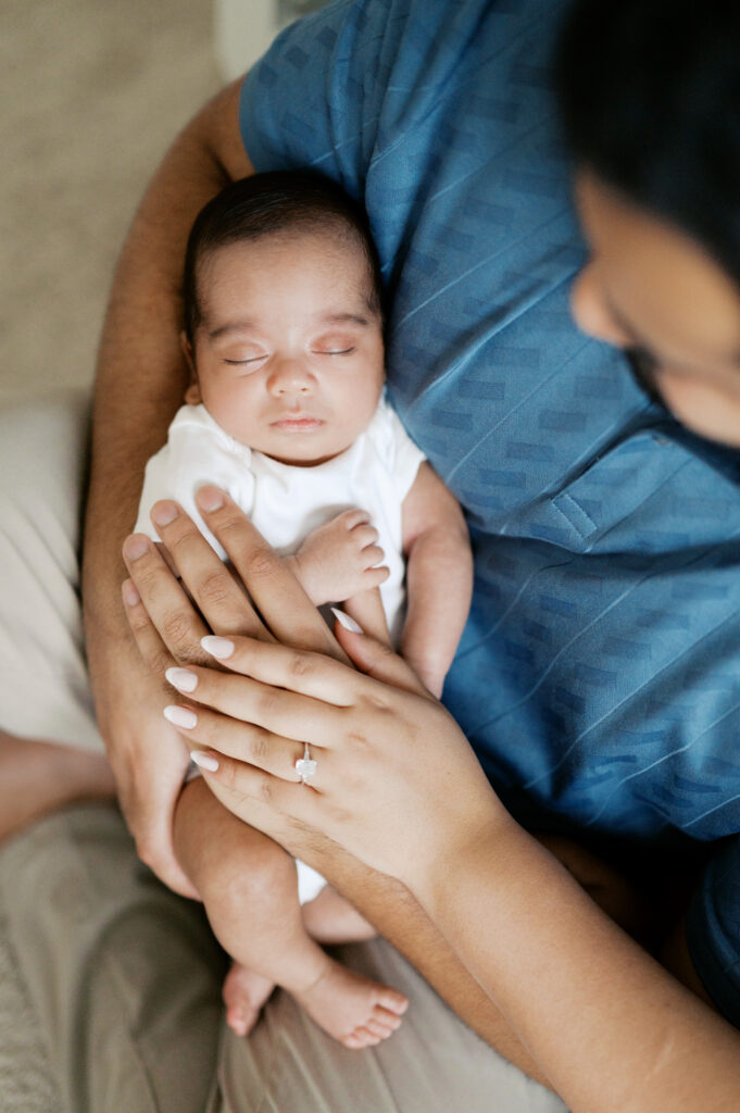 mom and dad lay hands on newborn baby in nursery