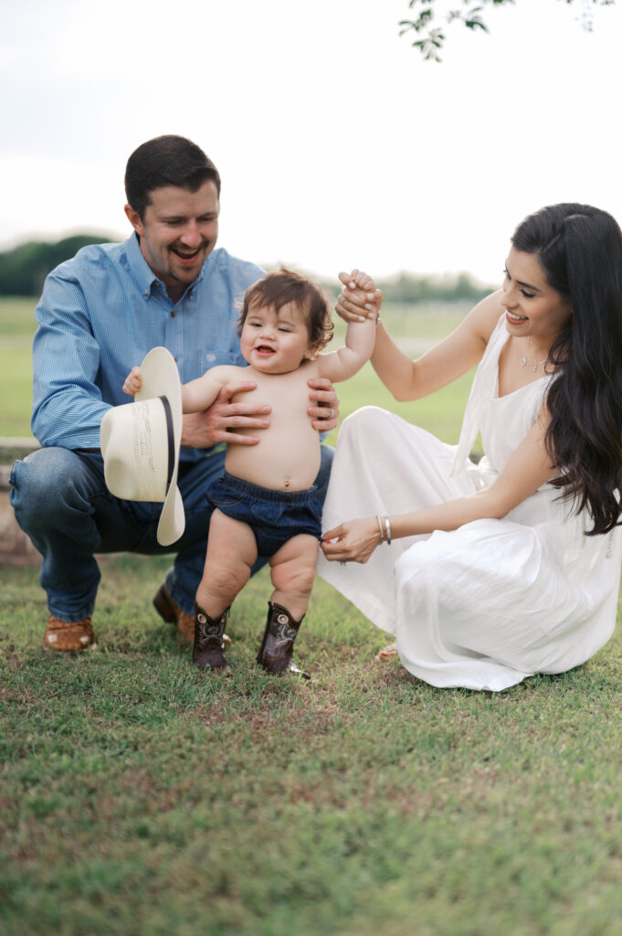 one year old smiles while parents hold him during family photos in benbrook