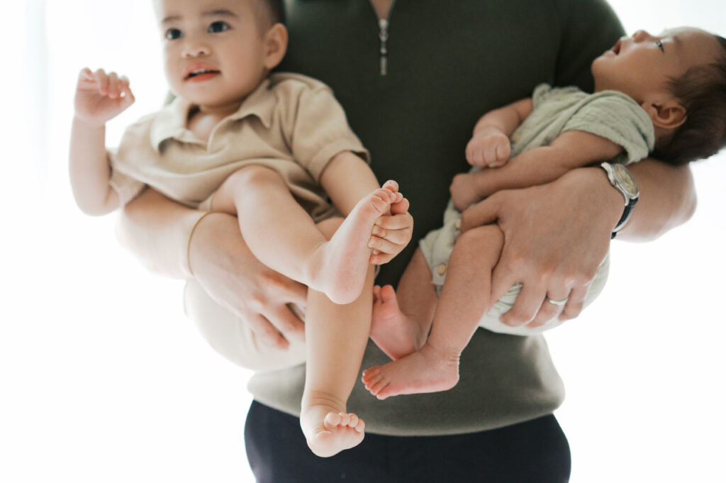 dad holds toddler boy and 2 month old newborn during newborn photos