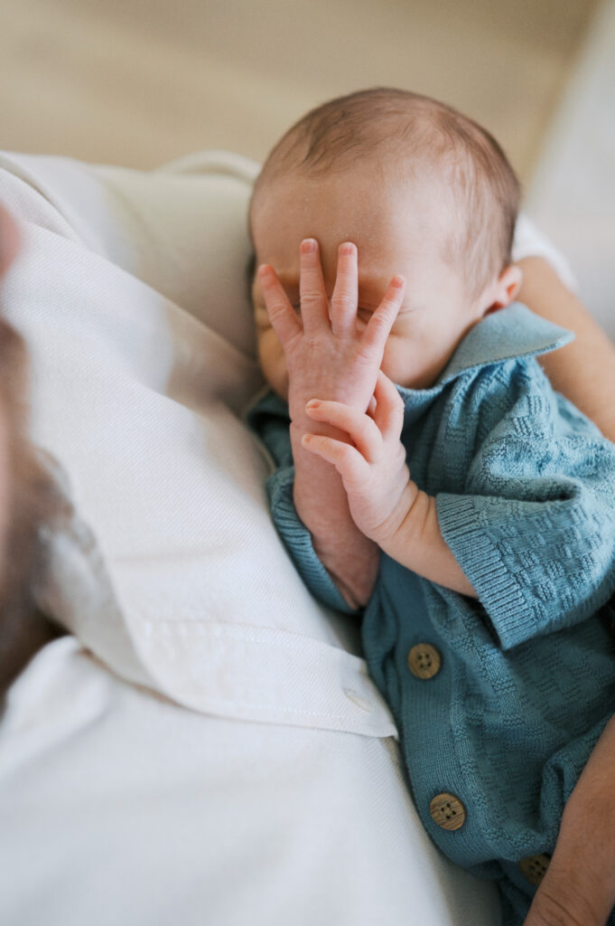 baby covers his face while snuggling in dad's arms