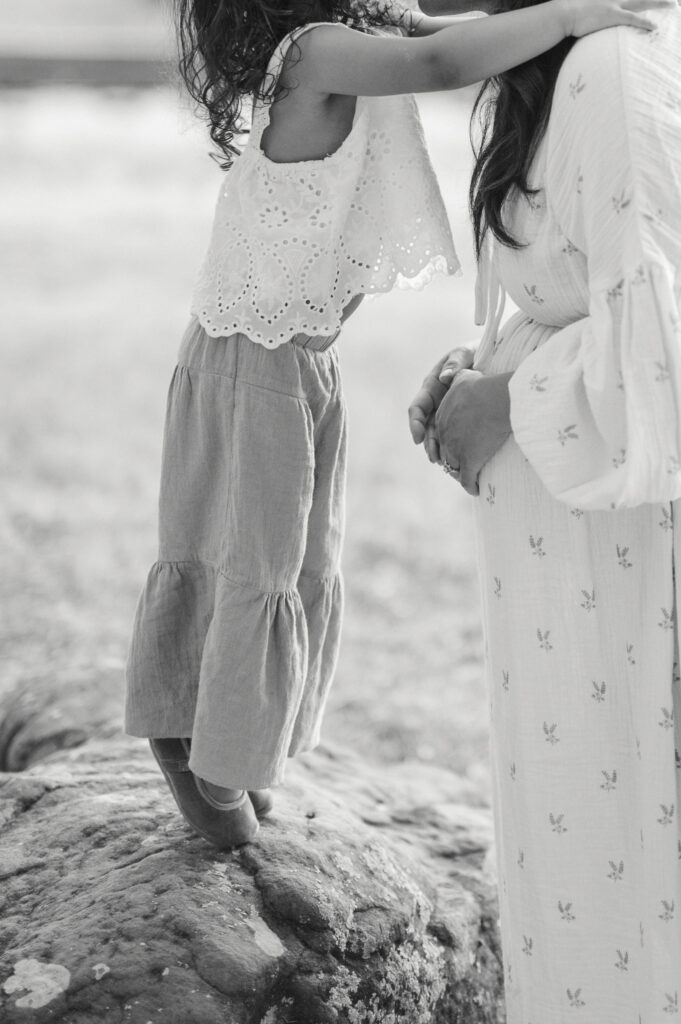 little girl hugs mom while mom holds baby bump