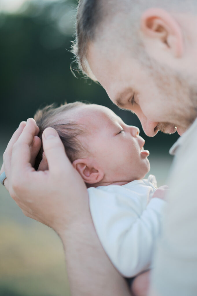 dad smiles while holding newborn baby boy close