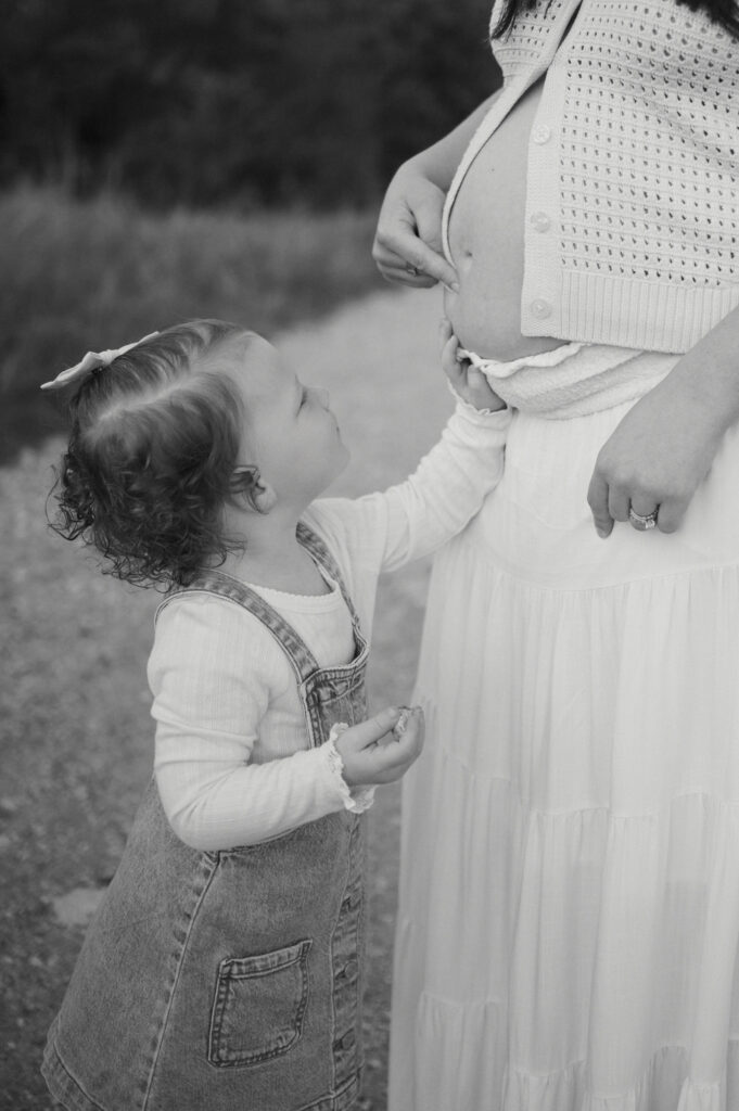little girl touches mom's expecting belly