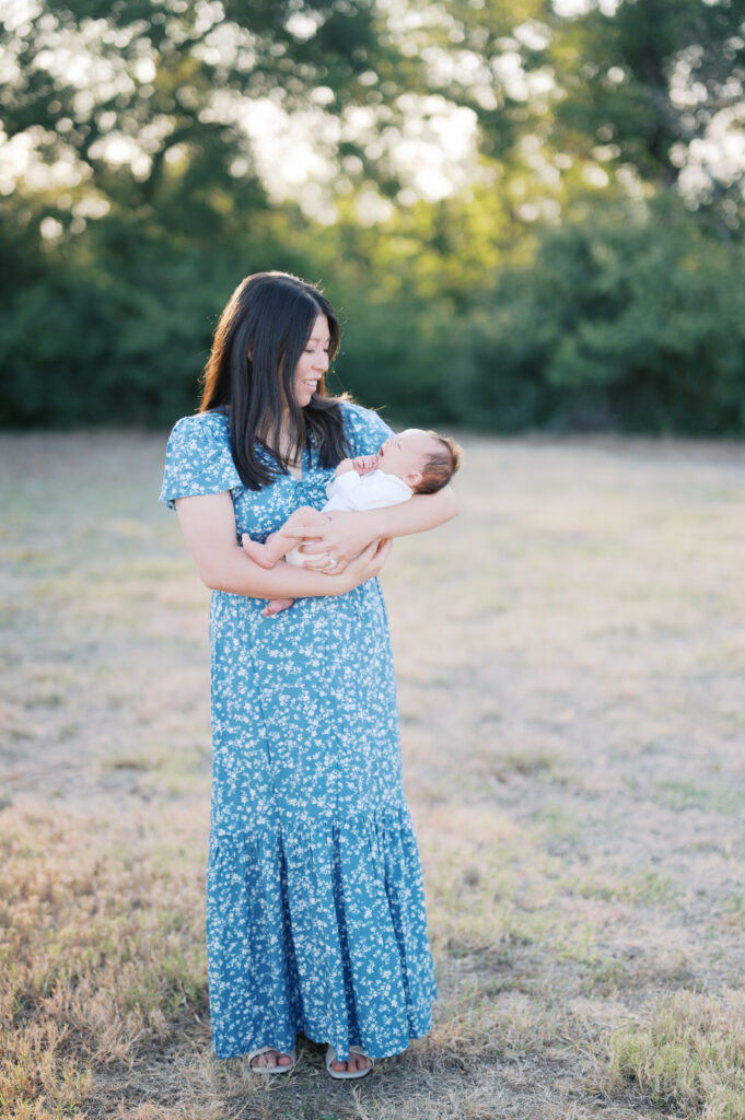 fort worth newborn photographer, outdoor newborn session, mom stands in field looking at baby