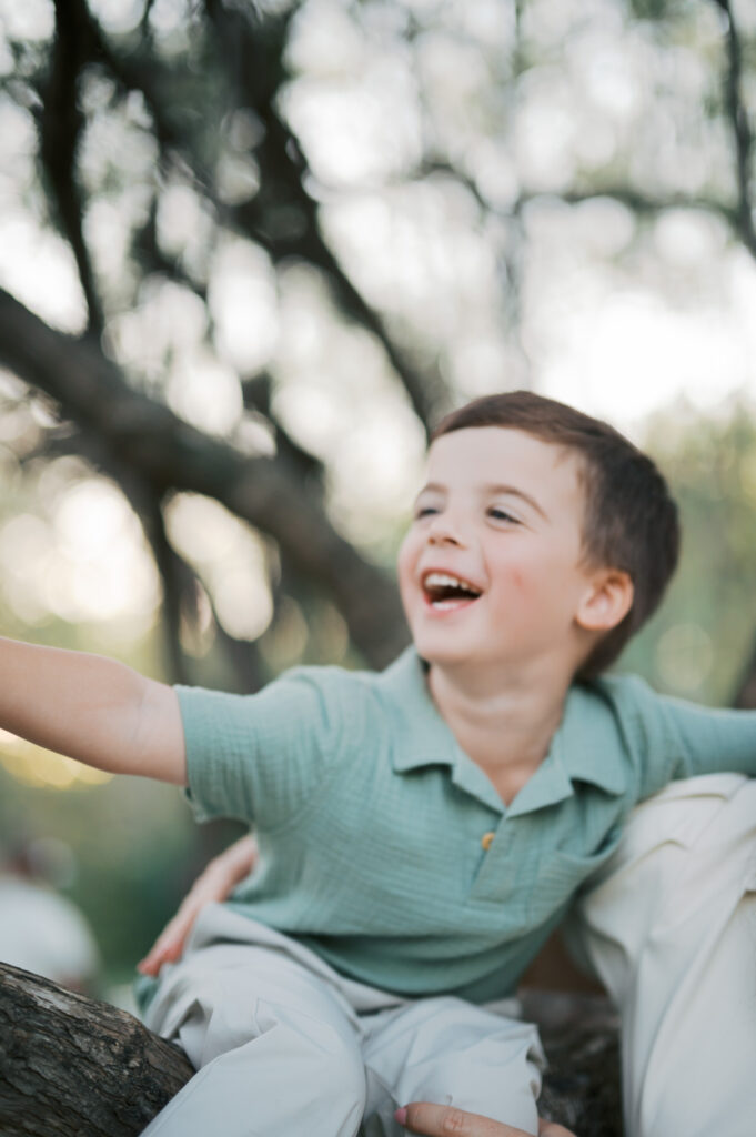 candid family photos, boy laughs while hanging out in a tree outdoors