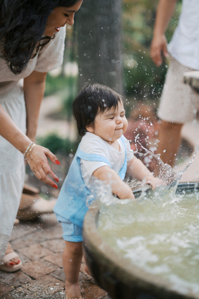 one year old splashes in water in backyard during one year old photo session in fort worth