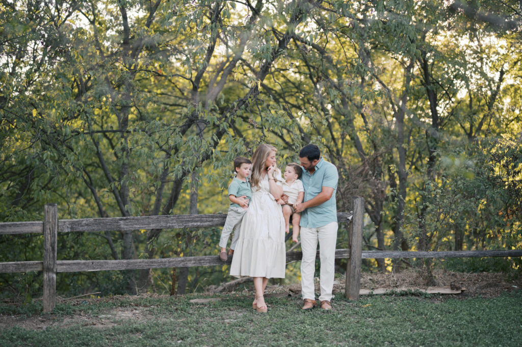 outdoor family photos in fort worth, family of four leans up against a fence