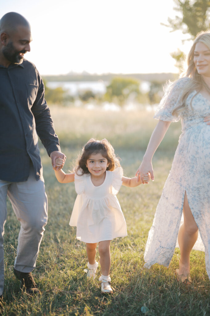 family of 3 walks, mom holds baby bump outdoors