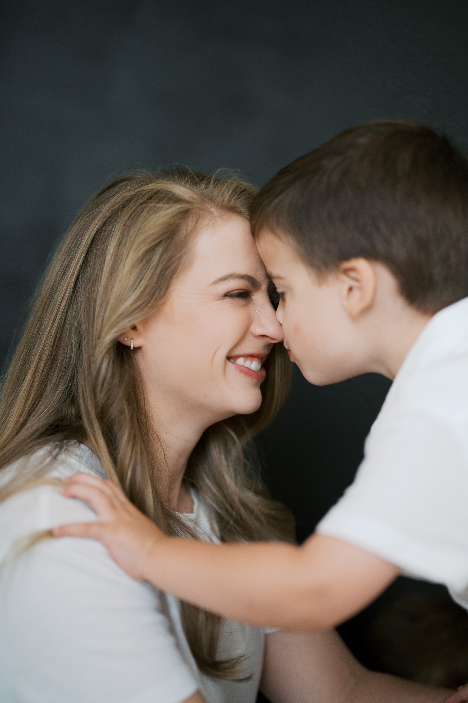 mom and snuggle cuddle close for family photos in a studio with black backdrop