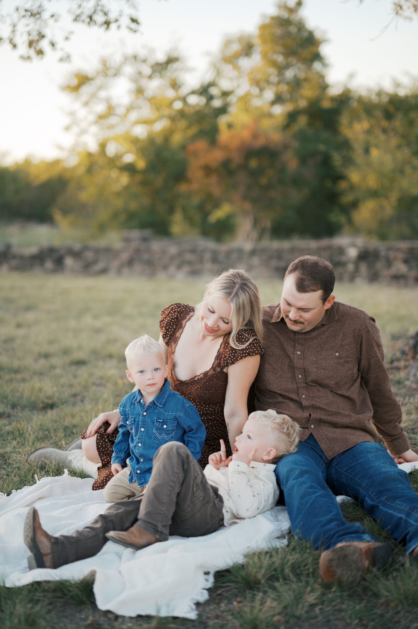 family gathers under a tree in the fall weather with their two boys