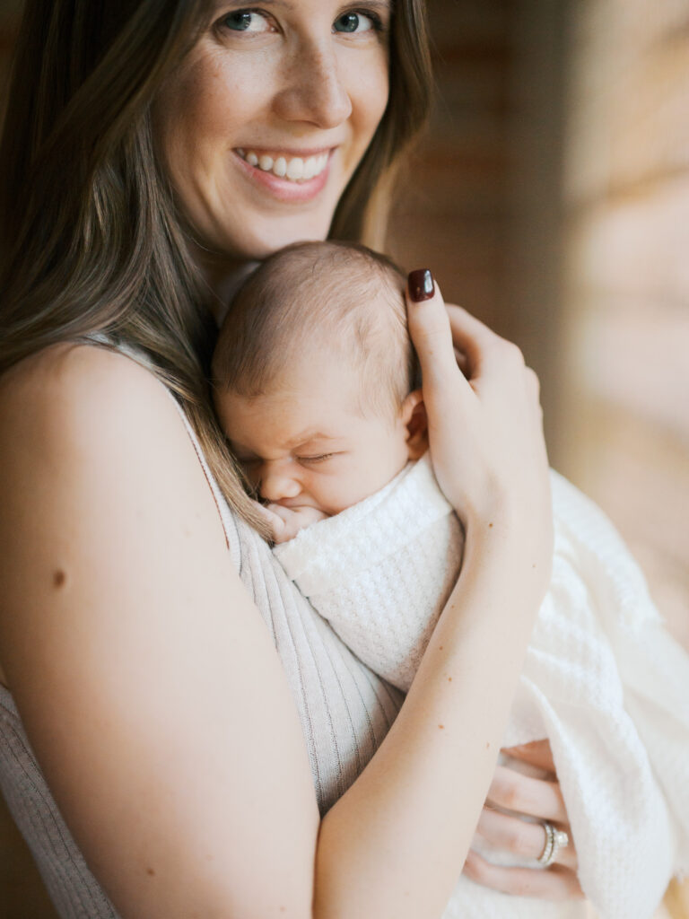 mom smiles at camera while baby snuggles during in home lifestyle newborn photos in fort worth